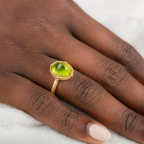 Gold ring with a peridot gemstone on a person's finger against a neutral background