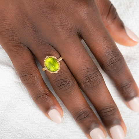 Gold ring with a peridot gemstone on a person's finger against a neutral background