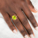 Gold ring with a peridot gemstone on a person's finger against a neutral background
