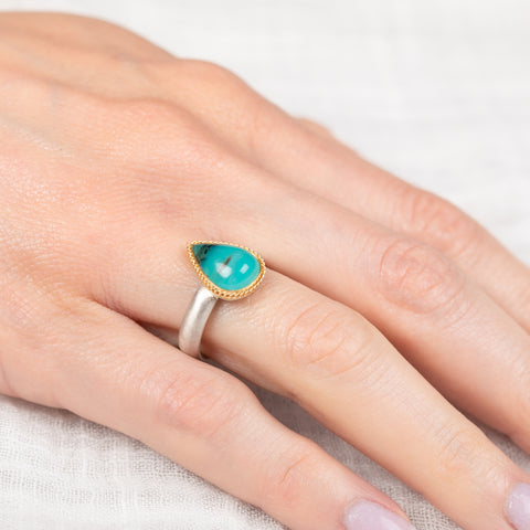 Silver and gold ring with a peruvian opal stone on a hand against a light background