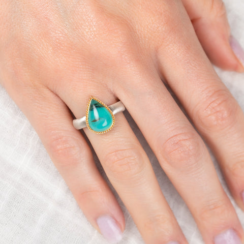 Teardrop-shaped peruvian opal gemstone ring on a hand with a white background