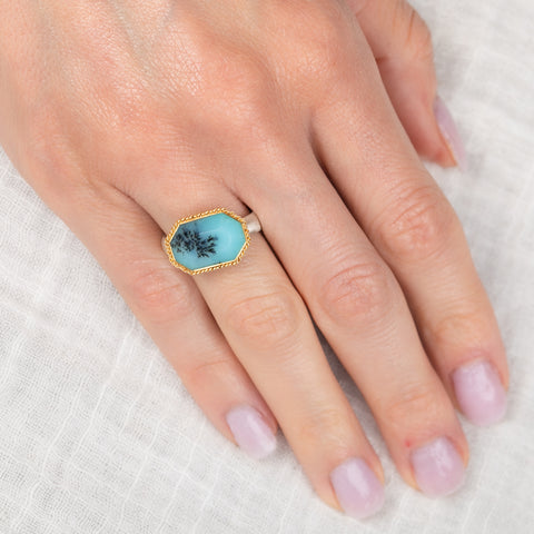 Hand wearing a ring with a peruvian opal gemstone on a white background