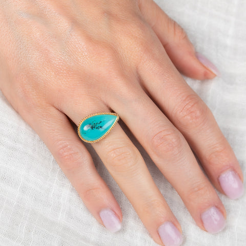 Hand wearing a peruvian opal ring with gold bezel and silver band on a white fabric background