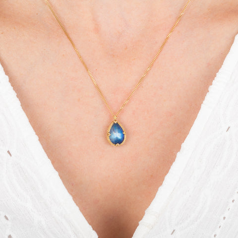 Gold necklace with a moonstone teardrop pendant on a person wearing a white top.
