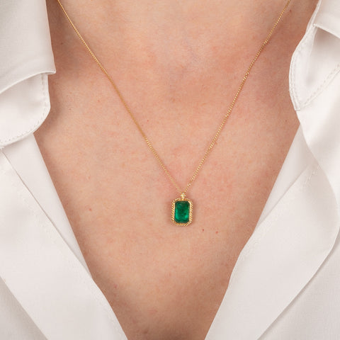 Gold necklace with a rectangular emerald gemstone pendant on a person