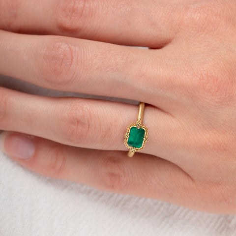 Gold ring with an emerald gemstone on a hand against a white background