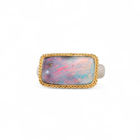 Ring with a boulder opal stone set in a gold bezel with a sterling silver band on a white background