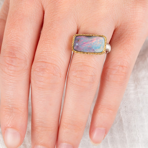 Hand wearing a boulder opal ring with gold bezel with a sterling silver band 