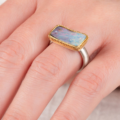 Close up of hand wearing a boulder opal ring with gold bezel with a sterling silver band 