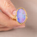 Gold ring with a colorful boulder opal stone held by a hand against a neutral background