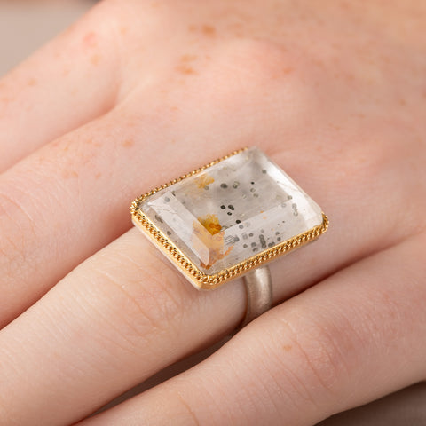 A person wearing a handmade fine jewelry ring featuring a pyrite in quartz gemstone with an 18k gold bezel and sterling silver band