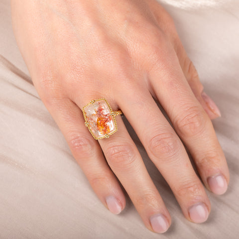 Hand wearing a gold ring with a colorful Quartz with Pyrite gemstone on a neutral background