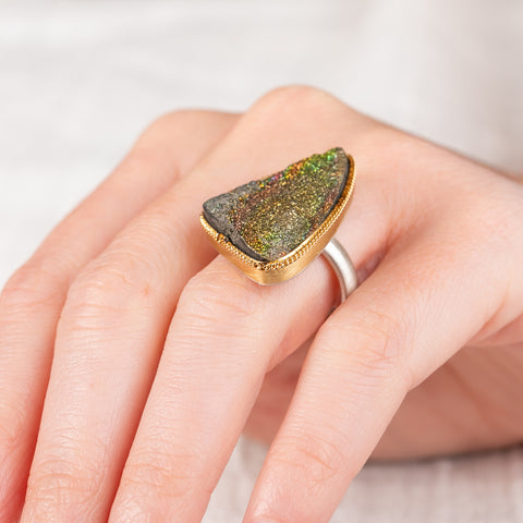 Close up of hand wearing a rainbow pyrite druzy ring with gold bezel and silver band