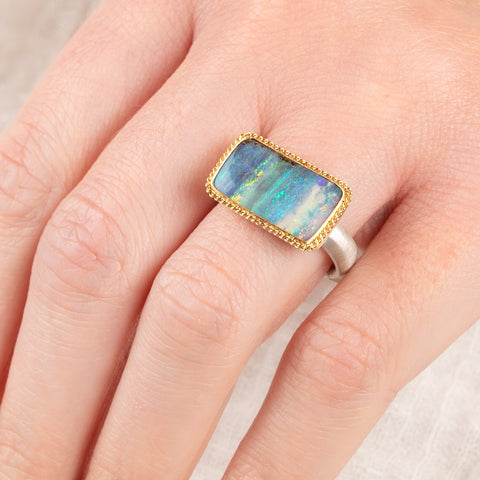 Close up of person wearing a handmade fine jewelry boulder opal ring with an 18k gold bezel and sterling silver band