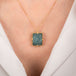 Gold necklace with an aquamarine gemstone pendant on a person wearing a white top.