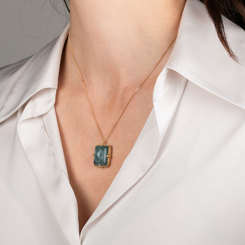 Gold necklace with an aquamarine gemstone pendant on a person wearing a white top.