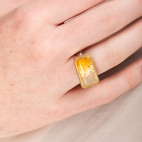 Gold and silver ring with a rectangular citrine stone on a person's hand