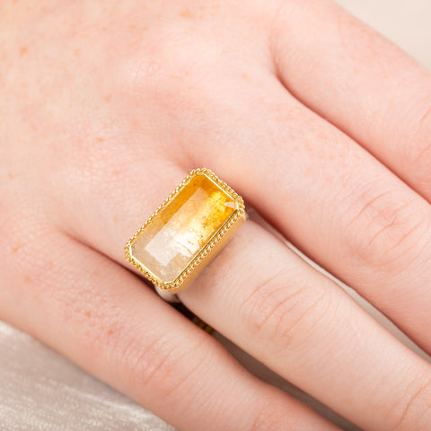 Gold and silver ring with a rectangular citrine stone on a person's finger