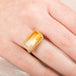 Gold and silver ring with a rectangular citrine stone on a person's finger