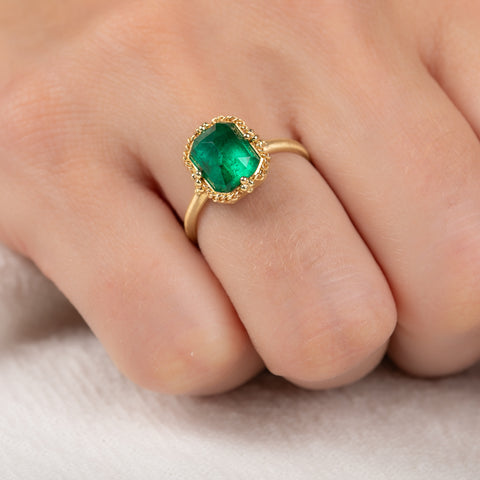 Gold ring with an emerald gemstone on a finger against a neutral background