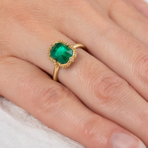 Gold ring with an emerald gemstone on a person's finger