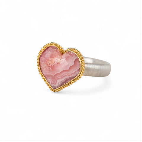 Heart-shaped ring with rhodochrosite stone, gold setting and silver band on a white background