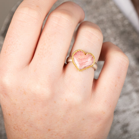 Heart-shaped ring with rhodochrosite stone, gold setting and silver band on a person's finger