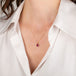 Gold necklace with a teardrop-shaped ruby pendant worn by a person in a white shirt.