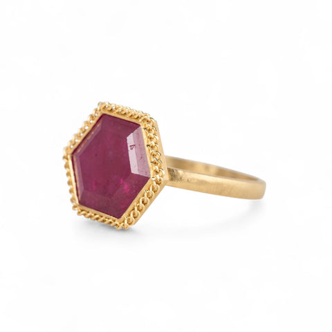 Gold ring with a hexagonal ruby gemstone on a white background