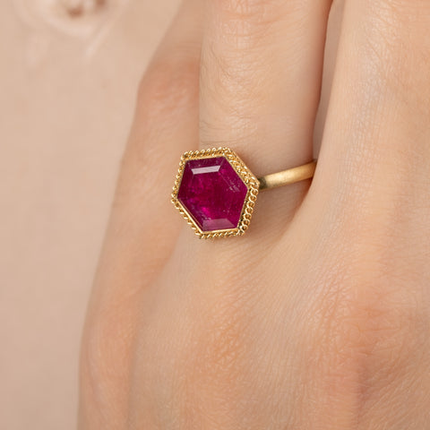Gold ring with a hexagonal ruby gemstone on a person's finger