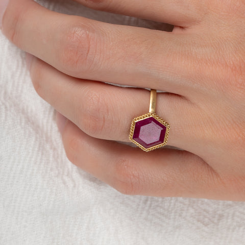 Gold ring with a hexagonal ruby gemstone on a person's finger