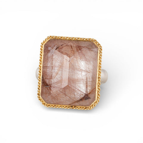 Ring with a gold bezel, silver band and rutilated quartz stone on a white background