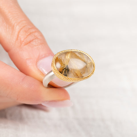 Ring with a gold bezel, silver band and rutilated quartz stone held in hand
