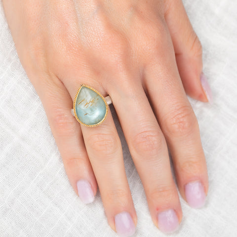 Hand wearing a gold and silver ring with a rutilated topaz gemstone on a white background
