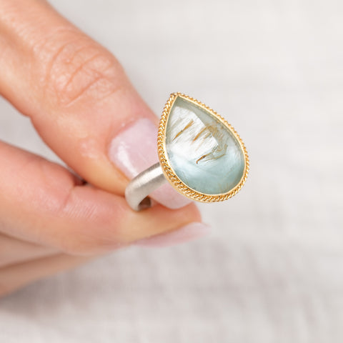 Teardrop-shaped gold and silver ring with rutilated topaz stone held in hand