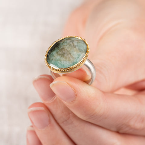 Hand wearing an Emerald ring with a gold bezel and sterling silver band