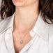 Gold necklace with an aquamarine worn by a person in a white shirt.