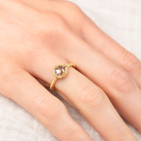 Gold ring with a diamond gemstone on a person's finger against a neutral background