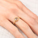 Gold ring with a diamond gemstone on a person's finger against a neutral background
