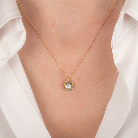 Gold necklace with a silver diamond on a person wearing a white shirt