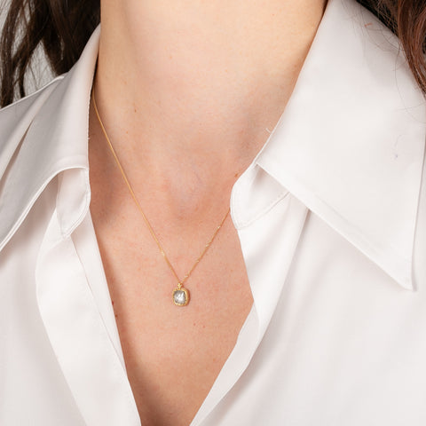Gold necklace with a diamond worn by a person in a white shirt
