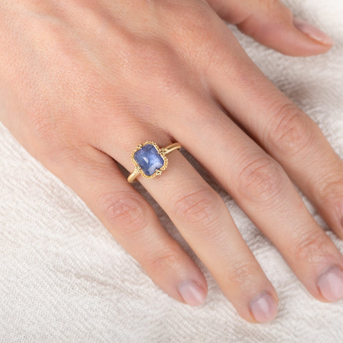 Gold ring with a blue tanzanite gemstone on a hand against a white background