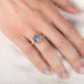 Gold ring with a blue tanzanite gemstone on a hand against a white background
