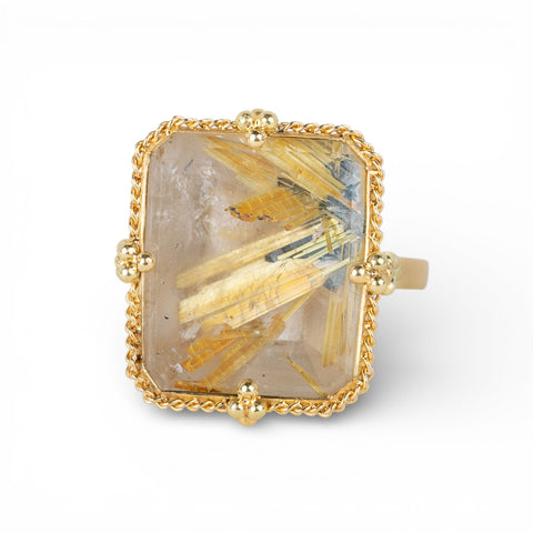 Gold ring with a large, faceted rutilated quartz stone on a white background