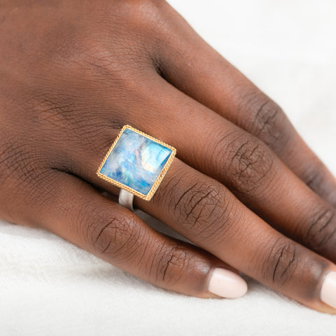 Gold and silver ring with a moonstone on a person's finger against a white background