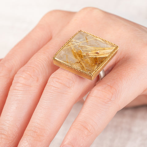 A close up of a hand wearing a handcrafted ring made with a rutilated quartz, 18k gold bezel and sterling silver band