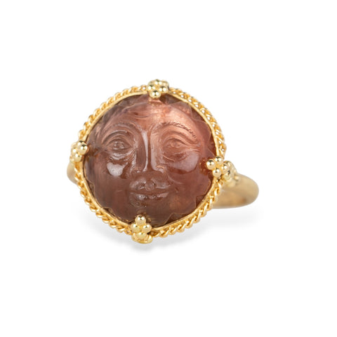 Gold ring with a face design carved into sunstone on a white background
