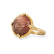 Gold ring with a face design carved into sunstone on a white background