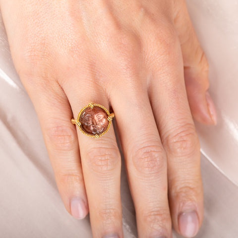 Gold ring with a face design carved into sunstone on a person's finger