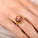 Gold ring with a face design carved into sunstone on a person's finger